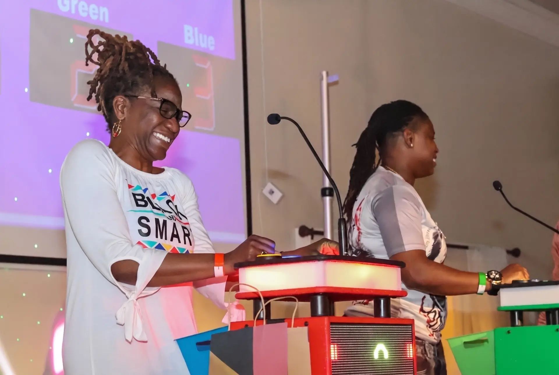 Two contestants laughing at their podiums in front of the game board screen